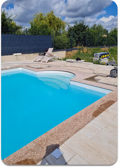 Moderner, sauberer Swimmingpool mit türkisblauem Wasser, umgeben von hellem Steinbelag und zwei weißen Liegestühlen bei bewölktem Himmel.